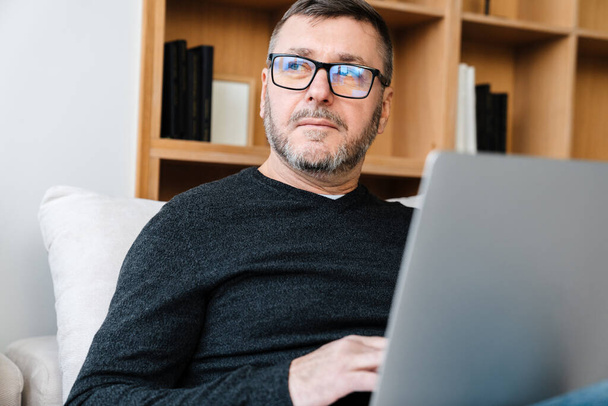 Serious adult unshaven man working with laptop while sitting at home - Photo, image