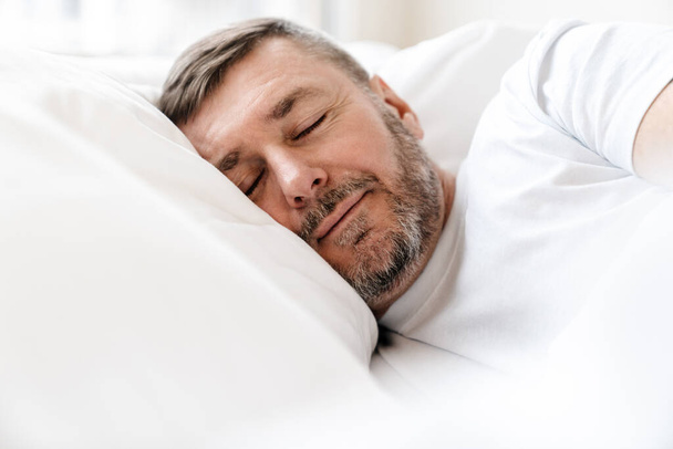 Peaceful adult unshaven man sleeping while lying in bed at home - Foto, imagen