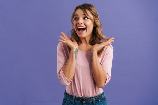 Portrait of a beautiful excited young casual woman standing isolated over blue background, celebrating - Foto, Imagen