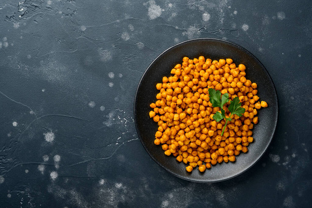 Fried chickpeas with turmeric with parsley and lime in black plate on an old black table background. Roasted spicy chickpeas or Indian chana or chole, popular snack recipe. Top view. - Foto, afbeelding