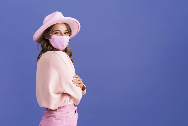 Joyful nice girl posing in protective mask and pink hat isolated over purple background - Foto, immagini