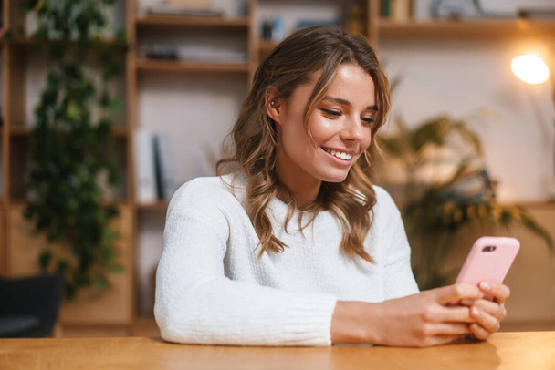 Close up de uma mulher atraente sorrindo usando telefone celular enquanto sentado no escritório moderno - Foto, Imagem
