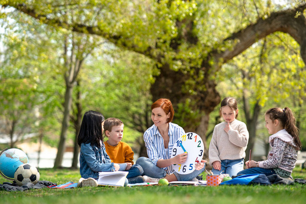Teacher with small children sitting outdoors in city park, learning group education concept. - Valokuva, kuva