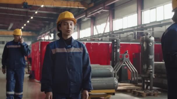 Sledování pomalosti sebevědomého ženského supervizora s dělníky v tvrdých kloboucích a kombinézách řídících práci na továrně - Záběry, video