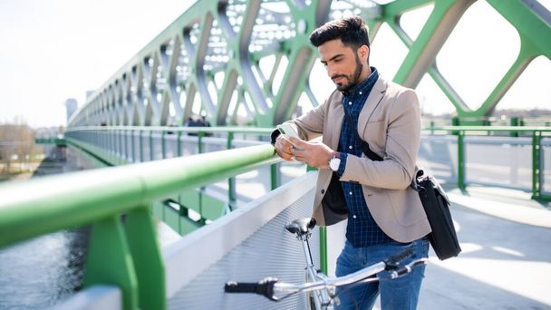 Young business man commuter with bicycle going to work outdoors in city, using smartphone. - Φωτογραφία, εικόνα