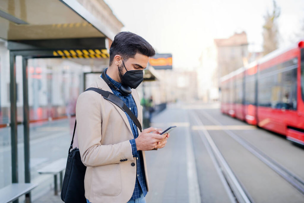Young business man commuter with smartphone on the way to work outdoors in city, coronavirus concept. - Foto, Imagen
