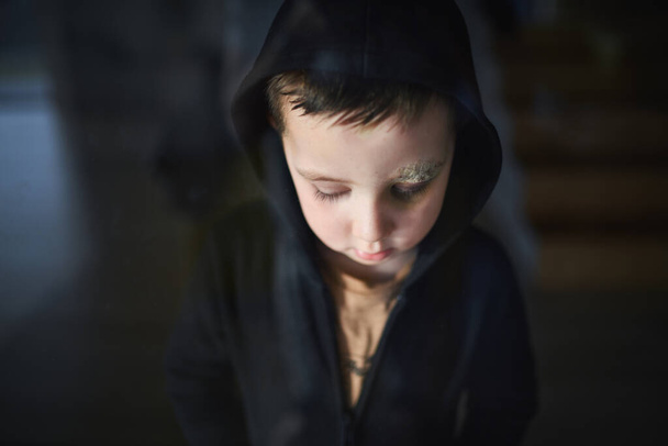 Close-up of sad small boy with cut eyebrow standing indoors at home, poverty concept. - Foto, imagen