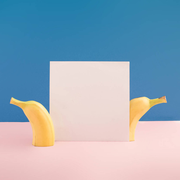 パステルピンクと青の明るい背景に新鮮なバナナとホワイトカードで最小限の果物やコピースペースの概念。創作料理のアイデア. - 写真・画像