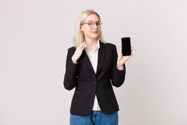 blond pretty woman looking arrogant, successful, positive and proud and holding a mobile telephone - Photo, Image