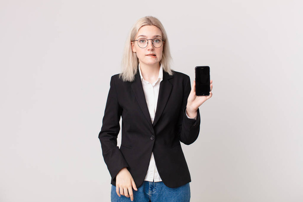 blond pretty woman looking puzzled and confused and holding a mobile telephone - Foto, imagen