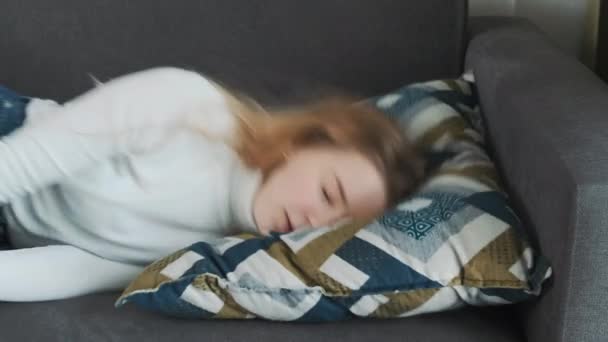 Mladá evropská vyčerpaná nebo znuděná žena po náročném pracovním dni doslova spadne na polštář pohovky a usne. - Záběry, video