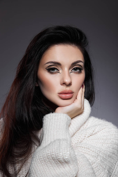 Beauty portrait of woman in white sweater, perfect evening makeup on dark background. Perfect skin without wrinkles, professional beauty makeup, long black hair - Photo, image