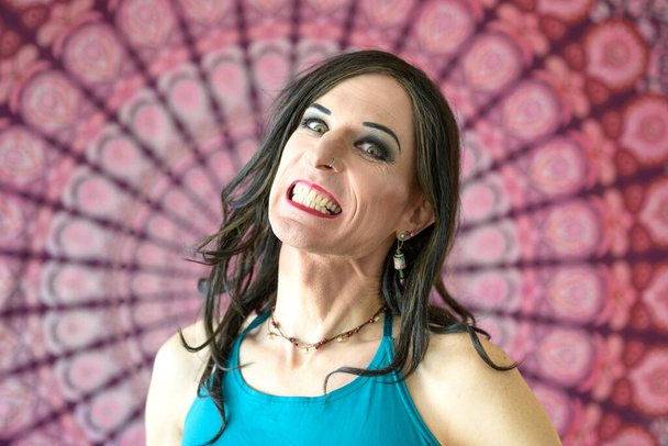 Porträt eines Transgender-Mannes, der seine Zähne vor buntem Hintergrund zeigt - Foto, Bild