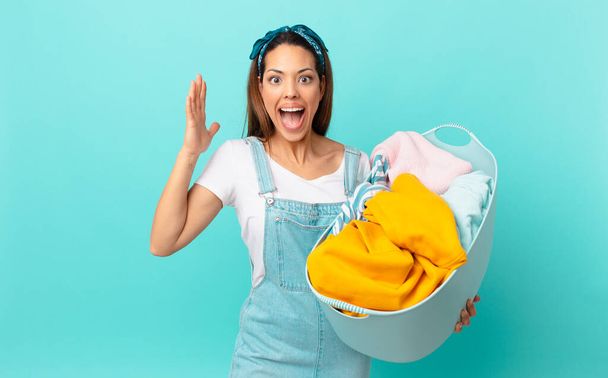 young hispanic woman feeling happy and astonished at something unbelievable and washing clothes - Φωτογραφία, εικόνα