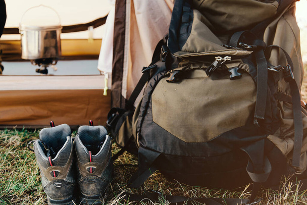 Close-up of hiking backpack and trekking boots against the background of a tourist tent. - 写真・画像