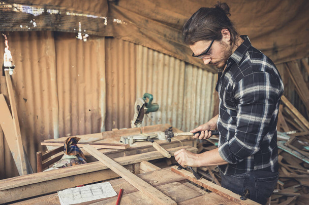 Erkek marangoz atölyedeki bir odun parçasına çekiç ve keski kullanıyor.) - Fotoğraf, Görsel