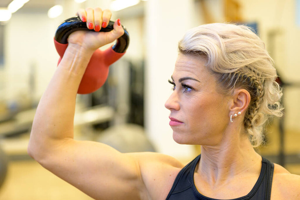 Подтянутая мускулистая женщина, тренирующаяся с килограммом веса в тренажерном зале в концепции здоровья и фитнеса, поднимая его над плечом крупным планом - Фото, изображение