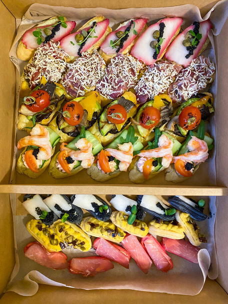 Коробка с маленькими бутербродами с холодными ломтиками, овощами на гриле, сыром и морепродуктами. Чаркутерические доски на заказ - Фото, изображение