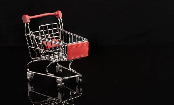Zbliżenie czerwony wózek sklepowy z refleksją na temat czarnego tła, handlu i koncepcji zakupów. - Zdjęcie, obraz