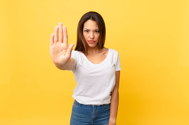 young hispanic woman looking serious showing open palm making stop gesture - Photo, image