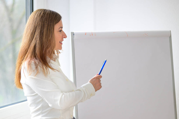 Donna d'affari che fa una presentazione indicando un flip board vuoto con la penna mentre parla in una parte superiore del corpo da vicino - Foto, immagini