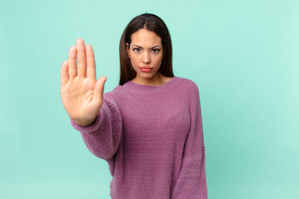young hispanic woman looking serious showing open palm making stop gesture - 写真・画像