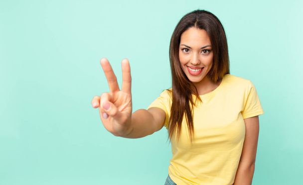 young hispanic woman smiling and looking happy, gesturing victory or peace - Photo, Image
