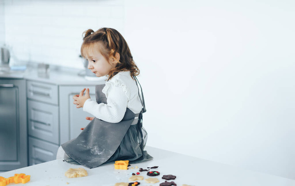 Kleines Mädchen kocht süße Plätzchen, sitzt auf dem Tisch. - Foto, Bild