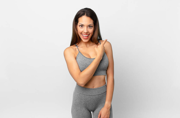 young hispanic woman looking excited and surprised pointing to the side. fitness concept - Photo, image