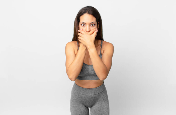 young hispanic woman covering mouth with hands with a shocked. fitness concept - Foto, Imagem