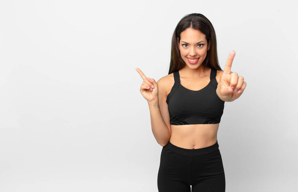 young hispanic woman smiling and looking friendly, showing number one. fitness concept - Фото, изображение