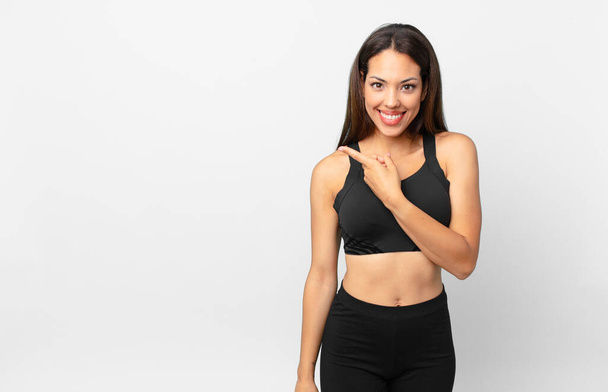 young hispanic woman smiling cheerfully, feeling happy and pointing to the side. fitness concept - Valokuva, kuva