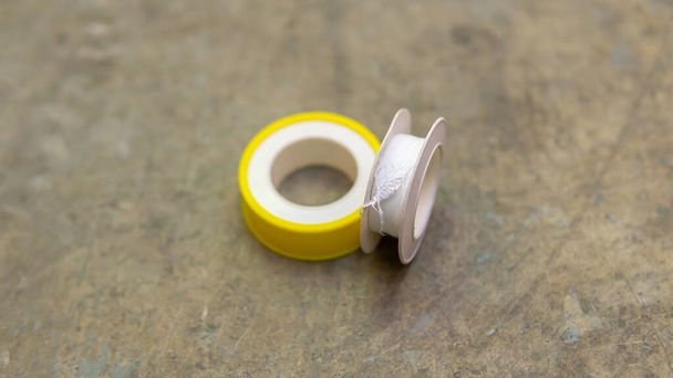 White tape or thread seal tape with yelloe casing on the floor. It is a polytetrafluoroethylene (PTFE) film tape commonly used in plumbing for sealing pipe threads. Selective focus on object. - Photo, Image