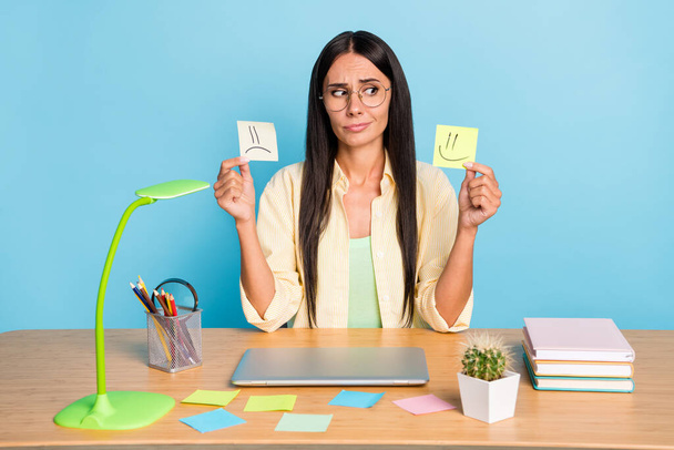 Photo of pretty lady sitting behind desk look curious hold sad happy stickers isolated on blue color background - Φωτογραφία, εικόνα