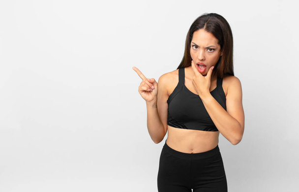 young hispanic woman with mouth and eyes wide open and hand on chin. fitness concept - Fotó, kép