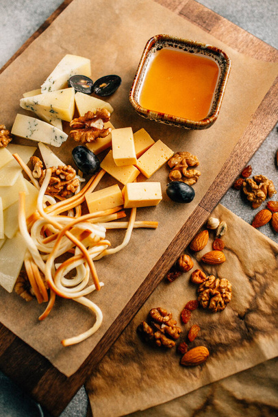 ξύλινη σανίδα με πιατέλα τυριού με σταφύλι και ξηρούς καρπούς με μέλι στο τραπέζι, κοντινή θέα  - Φωτογραφία, εικόνα