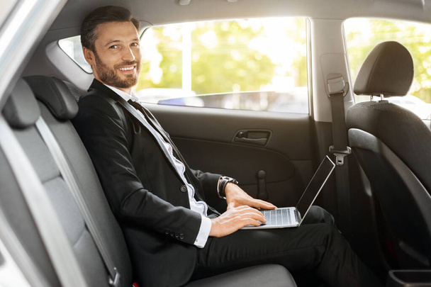 Cheerful businessman working on laptop while going to airport - Foto, Imagen