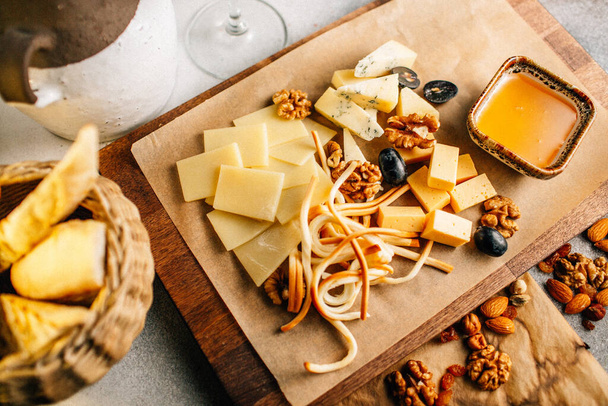 tabla de madera con plato de queso con uva y nueces con miel en la mesa, vista cercana  - Foto, imagen