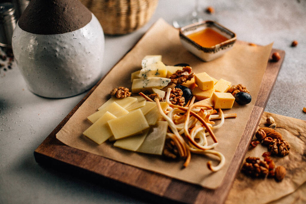 ξύλινη σανίδα με πιατέλα τυριού με σταφύλι και ξηρούς καρπούς με μέλι στο τραπέζι, κοντινή θέα  - Φωτογραφία, εικόνα