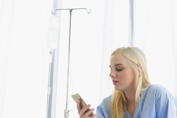 female patient holds the phone on the bed, the patient in the hospital room on day time - Fotografie, Obrázek