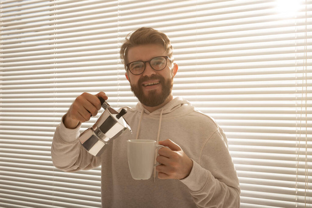 Young man pouring coffee from moka pot at morning. Breakfast and break concept. - Photo, Image