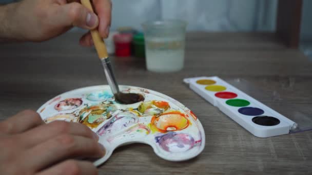 un hombre revolviendo pintura con un pincel en una paleta especial - Metraje, vídeo