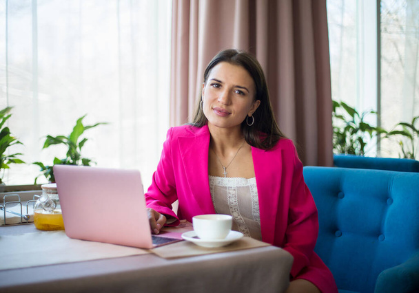 giovane donna in abito cremisi sedersi a tavola con tazza di tè e laptop nel ristorante - Foto, immagini