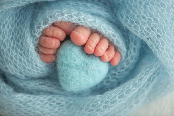 Dois lindos e pequenos pés de bebé embrulhados num cobertor de malha azul-verde. E um coração de malha feito de fios de lã. - Foto, Imagem