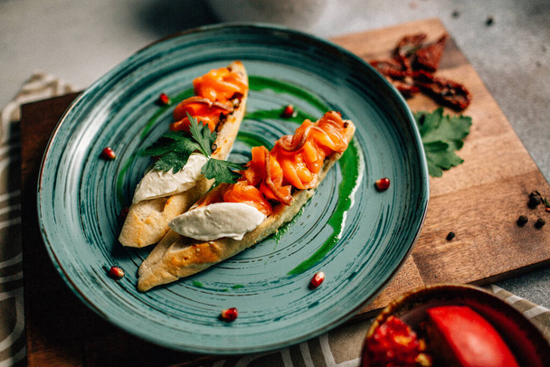 talíř s mini bruschettas a lososem s jemným mascarpone sýrem a granátovými semínky na dřevěné řezací desce, zblízka  - Fotografie, Obrázek
