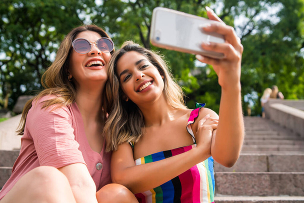 Two friends taking selfie with phone outdoors. - Zdjęcie, obraz