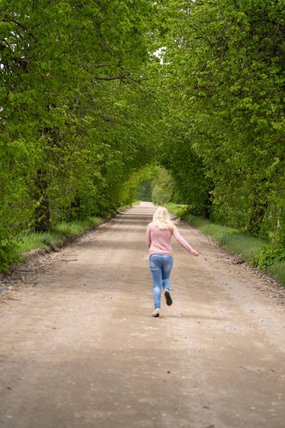 道路上の少女ブロンドは木のアーチで走り、緑 - 写真・画像