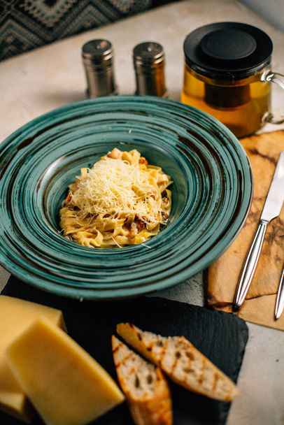 tészta sajttal a tányéron teáskanna mellett az asztalon - Fotó, kép