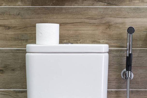 Moderni kylpyhuoneen sisustus, jossa on valkoinen keraaminen wc-säiliö, jossa on wc-paperi, ja kosketa seinää vasten puun kuviorakenteella taustalla - Valokuva, kuva