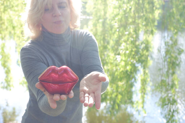 Девушка дует в поцелуй большими красными декоративными губами. Всемирный день поцелуя. - Фото, изображение